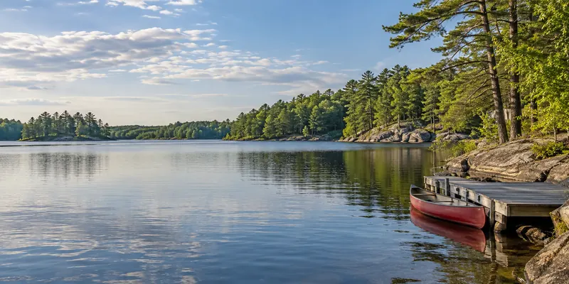 A red canoe beside a wooden dock on a quiet mixed-forest lake.