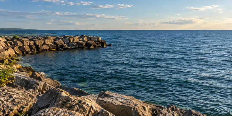 Blue freshwater to the horizon beside a low stone breakwater in warm light.