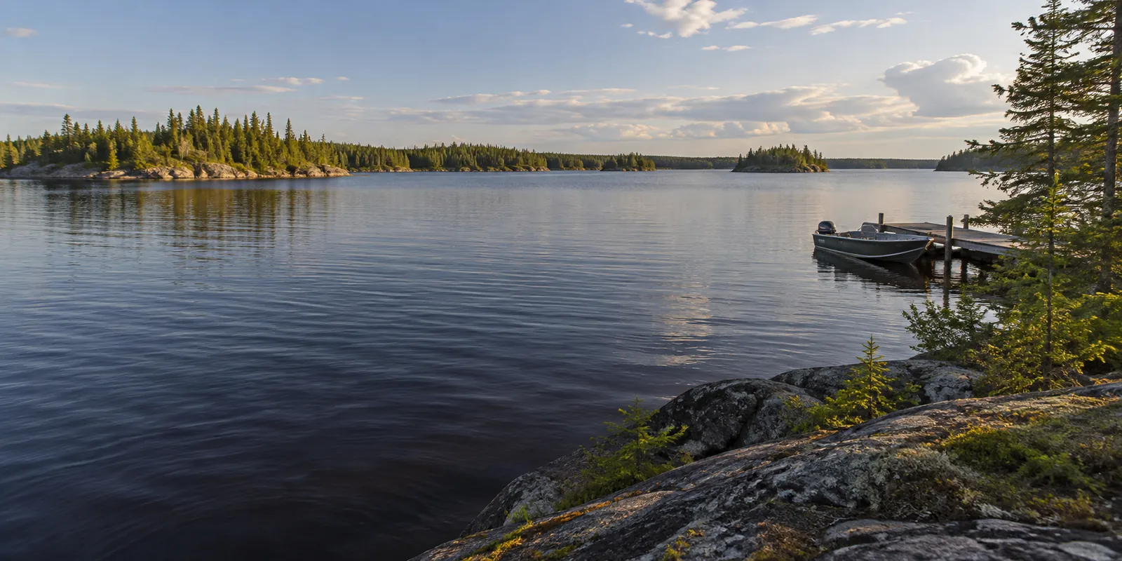 Wide lake with a low wooded shore and a moored boat in evening light
