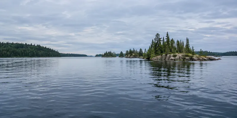 Low pine-covered islands and granite points across a broad blue lake.